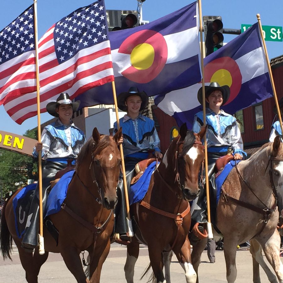 United States and Colorado flags wave in the wind as Buffalo Bills Day paraders ride on horseback up Washington Avenue in downtown Golden, Colorado.