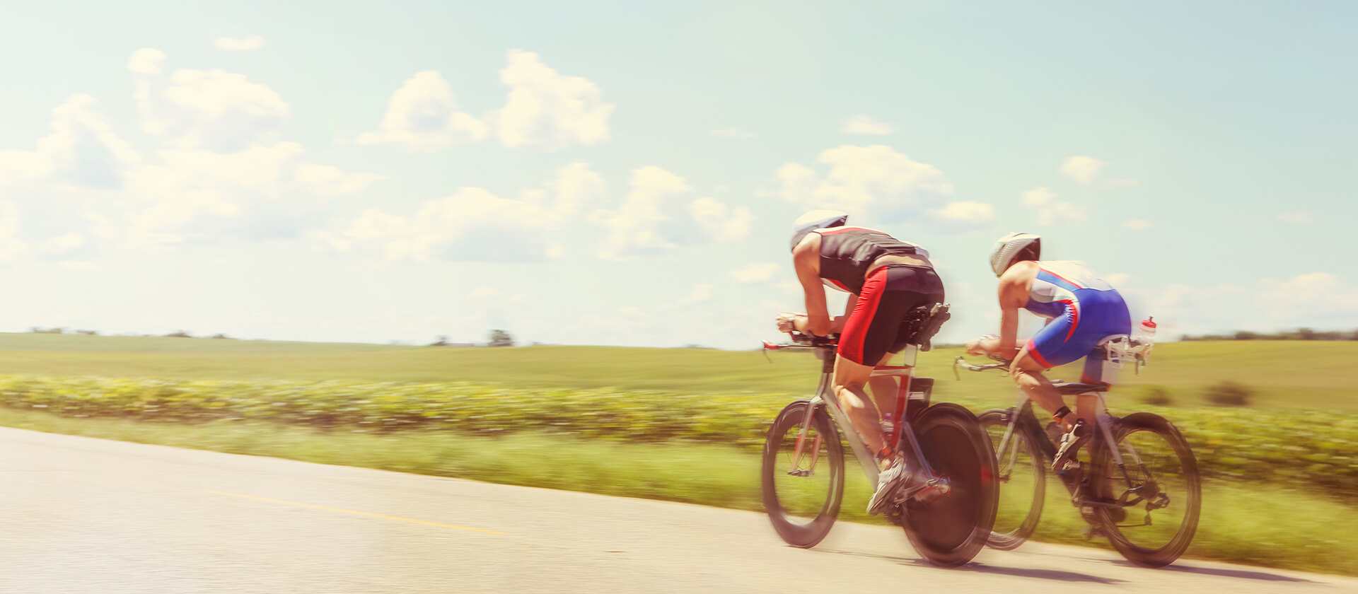 Cyclists riding down a paved road on a sunny day.
