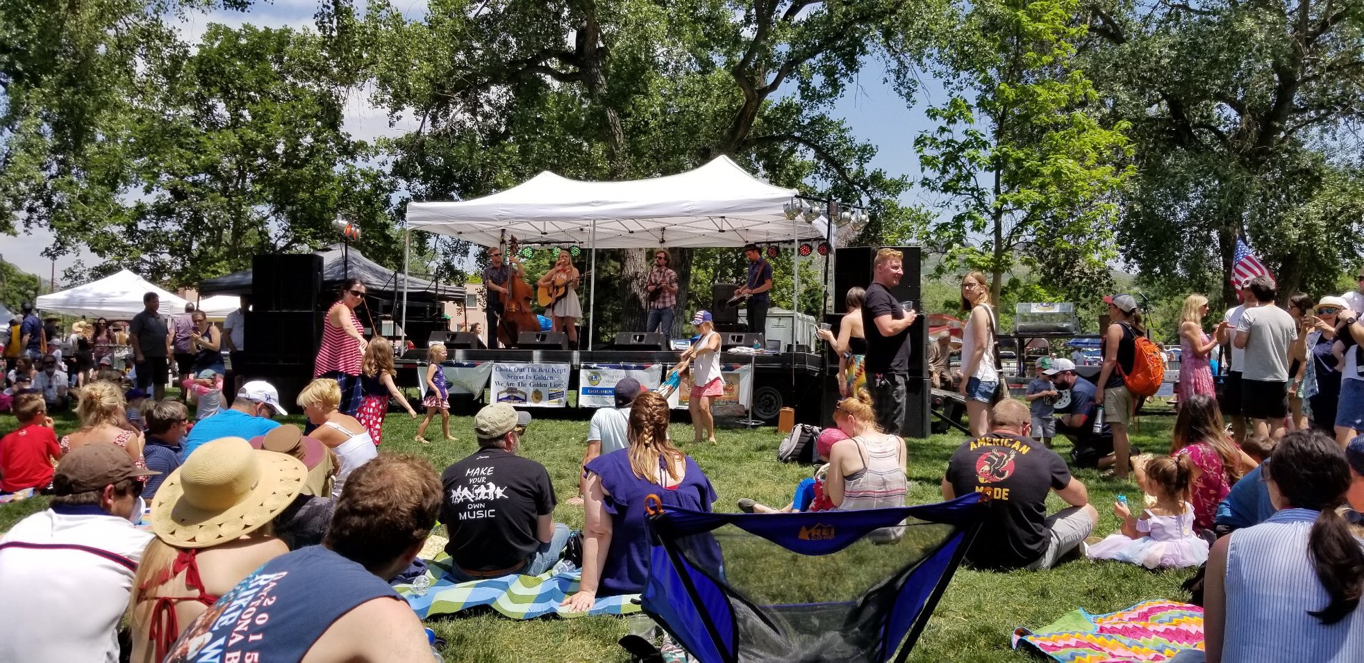 People sitting in Lions Park, downtown Golden Colorado listening to live music for the Golden Lions Club 4th of July celebration.